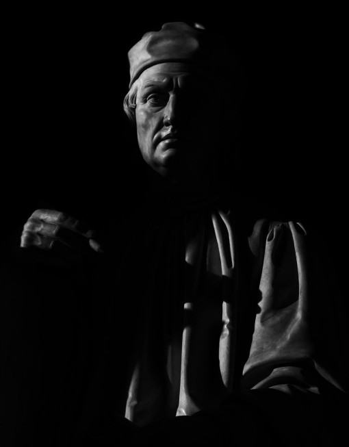 Black and white photograph of a sculpture of Arnolfo di Cambio. Taken in the morning light by the Duomo in Florence, Italy 